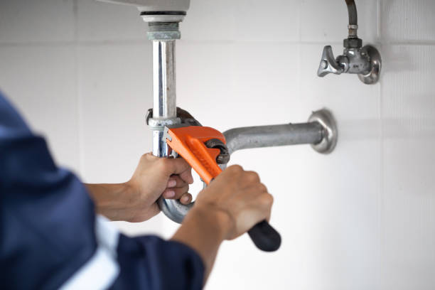 A plumber repairs a pipe below a sink.